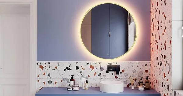 Specchio tondo con luce calda sopra un lavabo e una parete in graniglia
